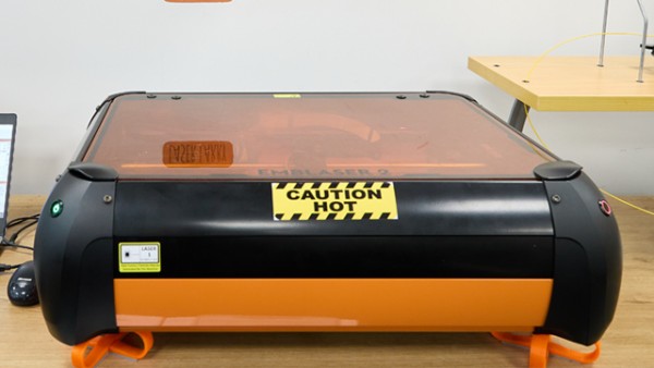 Laser Larry has is an Emblaser 2, a machine in orange colour with a bold sticker that says 'caution: hot'.