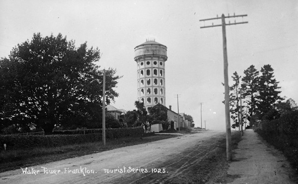 Concrete water tower next to dirt street.