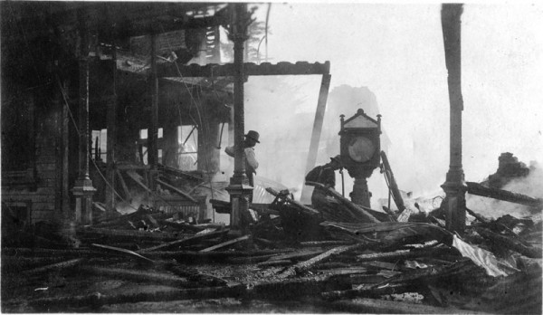 A black and white image showing two men examining a building destroyed by fire.