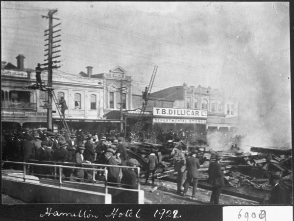 A black and white image showing a crowd gathered looking at a building ruined by fire.