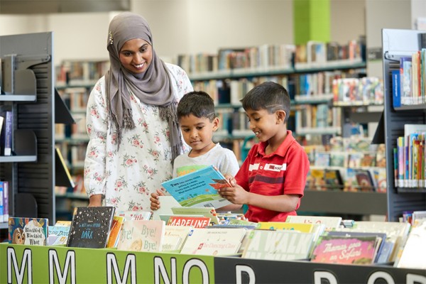 Mum with two little boys browsing for picture books at the library.