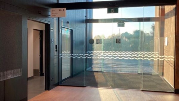 Two sets of double automatic doors, looking from inside out. Directly to the left is the entrance to the toilet facilities.