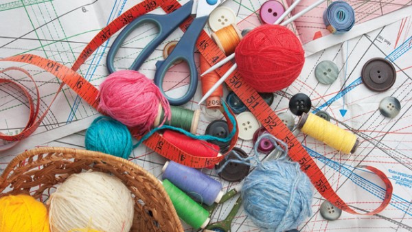 A jumble of assorted craft supplies, including balls of yarn, thread spools, buttons, knitting needles, scissors, and measuring tape.