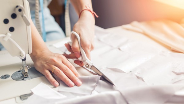 Person cutting some fabric next to a sewing machine.