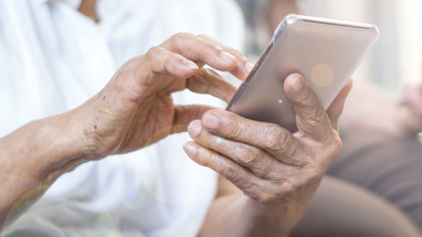 Close-up photo of a pair of hand belonging to an older person, holding and using a smartphone.