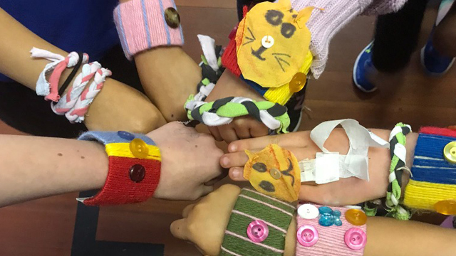 Children's hands wearing homemade upcycled wristbands made with fabric, buttons, and ribbons.