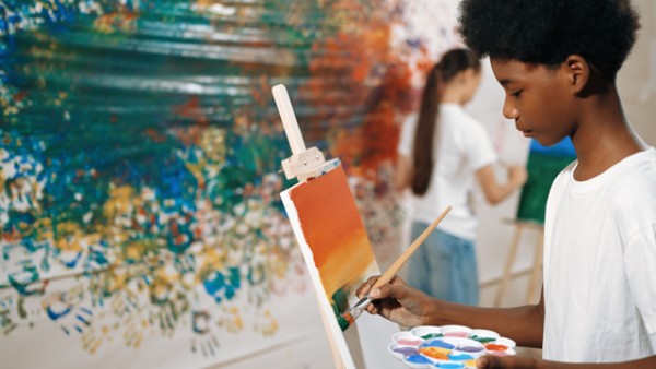 a child reaching out with a paint brush to palette.